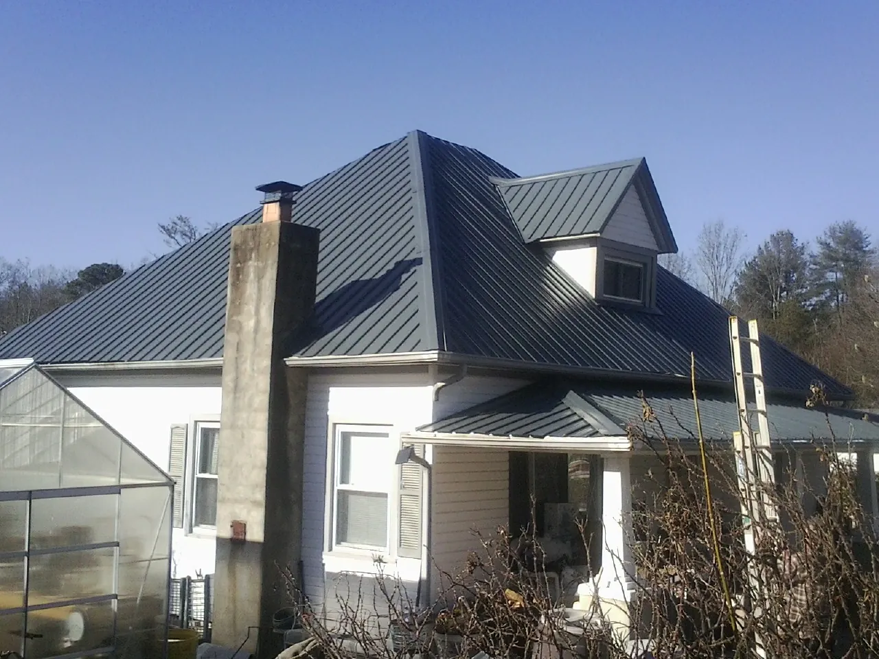Dark blue standing seam metal roof on a white farmhouse with dormer — Slate & Tile Roof Repair by Roofing Brothers in Bettendorf