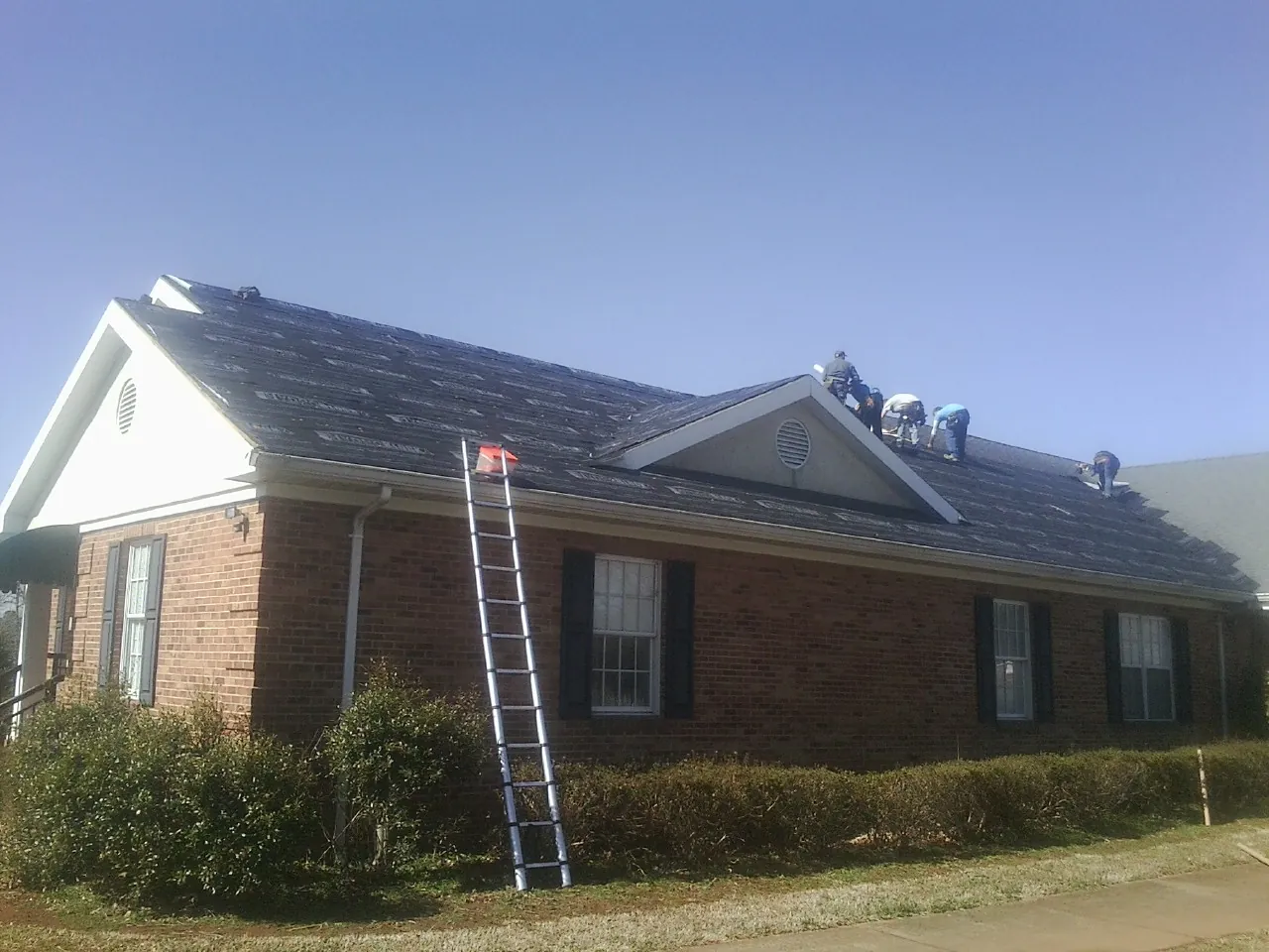 Crew tearing shingles off a brick ranch roof with a ladder set — Metal Roof Repair work by our crew in Bettendorf