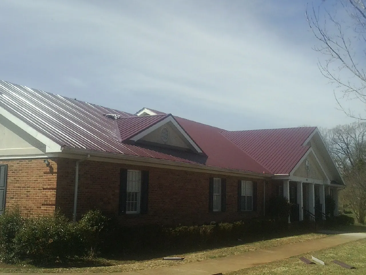 Red metal roof with gabled entries on a long brick building, from a Hail Damage Roof Repair job in Bettendorf