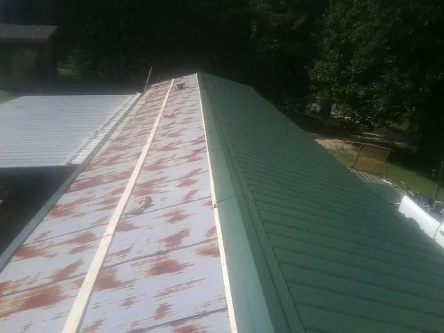 Old rusted panels beside newly installed green metal roofing — Wind Damage Roof Repair by Roofing Brothers in Bettendorf