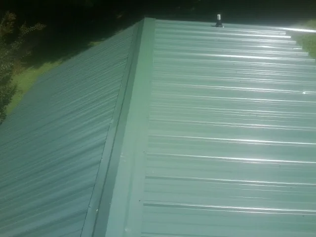 New green metal panels meeting at the ridge of a roof — Flat Roof Repair work by our crew in Bettendorf