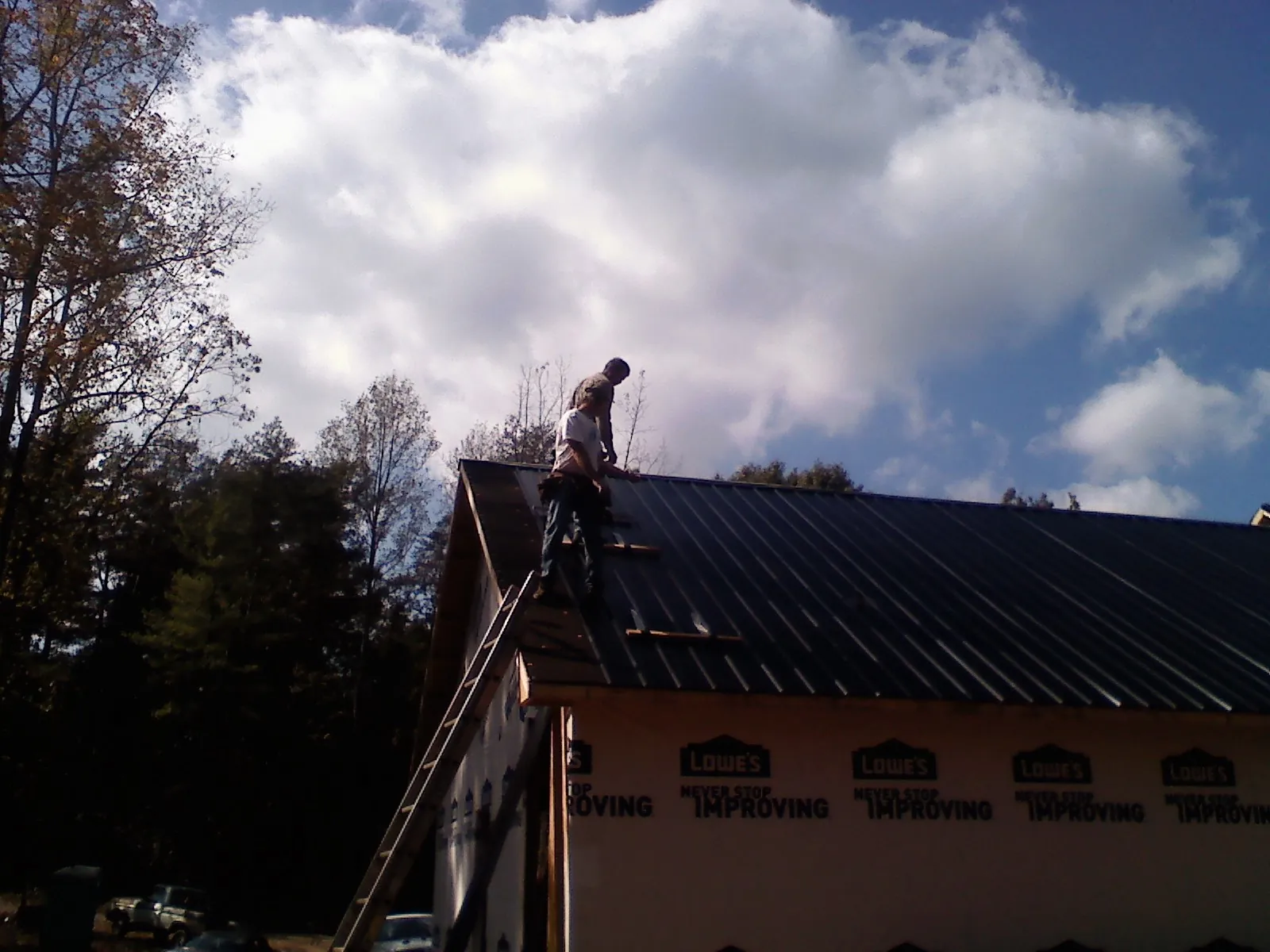Roofer fastening dark metal panels high against a cloudy sky, from a Roof Inspection job in Bettendorf