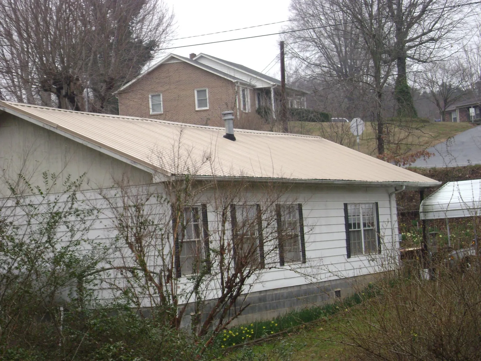 Tan metal roof on a white sided house set into a hillside — Commercial Roofing by Roofing Brothers in Bettendorf