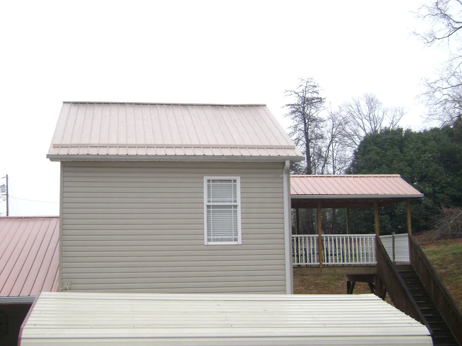 Tan metal roofs on a two story addition and attached porch, from a Roof Replacement job in Bettendorf
